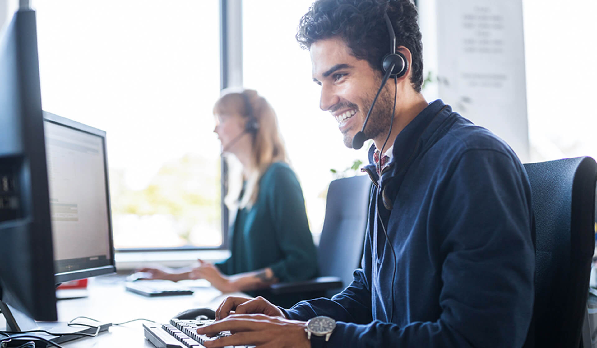 Smiling customer service representative with headset using computer at desk